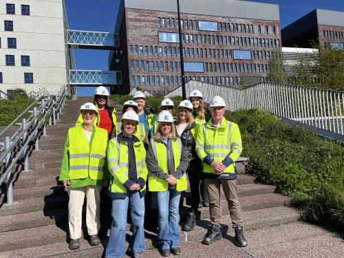 groepsfoto_van_het_back-officeteam_building_technics_north_met_veiligheidshelmen_en_fluohesjes_op_een_trap_voor_de_gebouwen_van_ku_leu.jpg