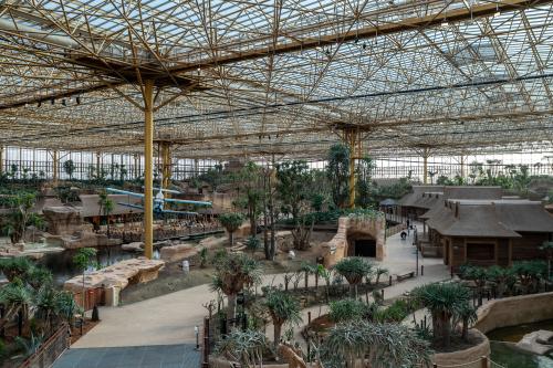 panoramisch_overzicht_van_edenya_met_wandelpaden_rietgedekte_gebouwen_waterpartij_en_het_vliegtuigdecor_onder_het_uitgestrekte_vakwerkdak.jpg